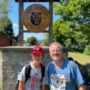 A Scout and adult Scout leader pose in front of the Camp Gorton sign in the summer sun
